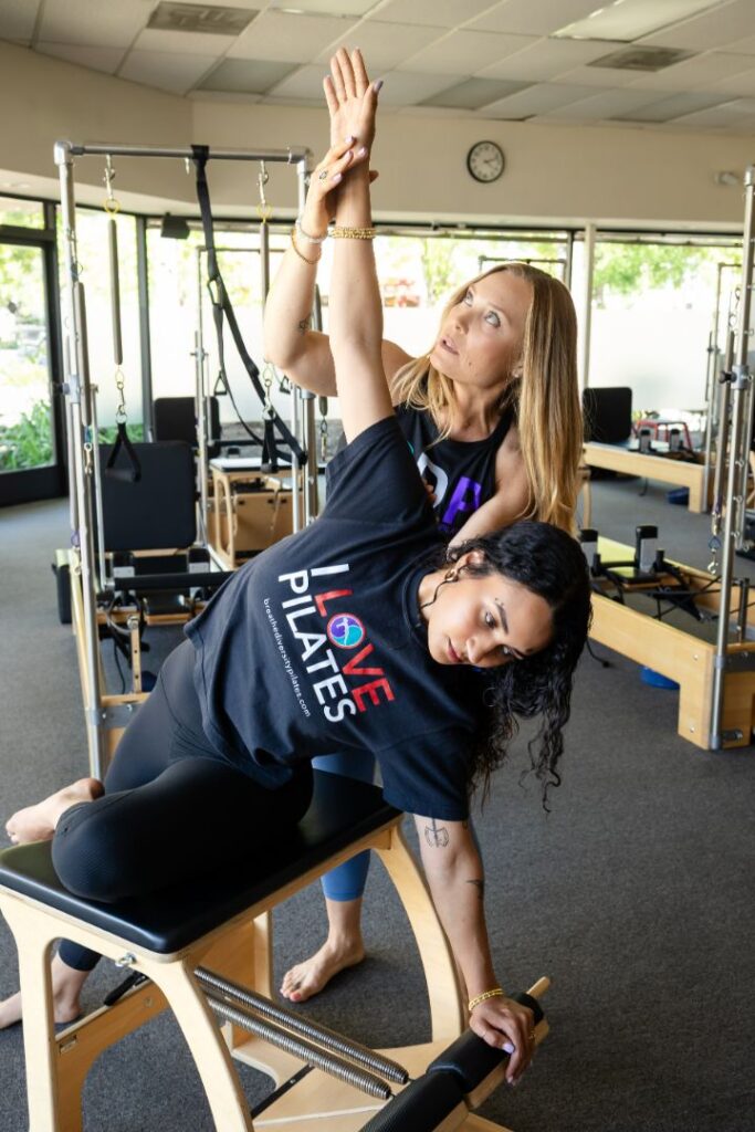 Pilates instructor assists client with side stretch on reformer.