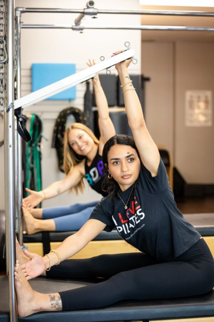 Two women stretching on Pilates reformer machines